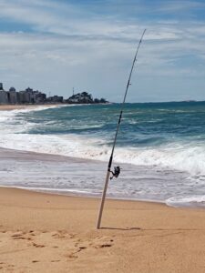 Caña de pescar con carrete clavada en la arena de la playa