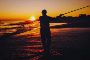 Silueta de un pescador con caña de surfcasting al atardecer